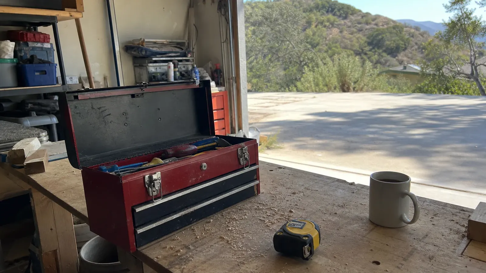 Open toolbox and tape measure on a garage workbench looking out at a Malibu canyon