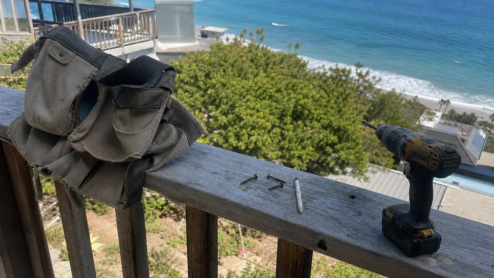 Tool belt and cordless drill on a weathered deck rail above the ocean in Malibu